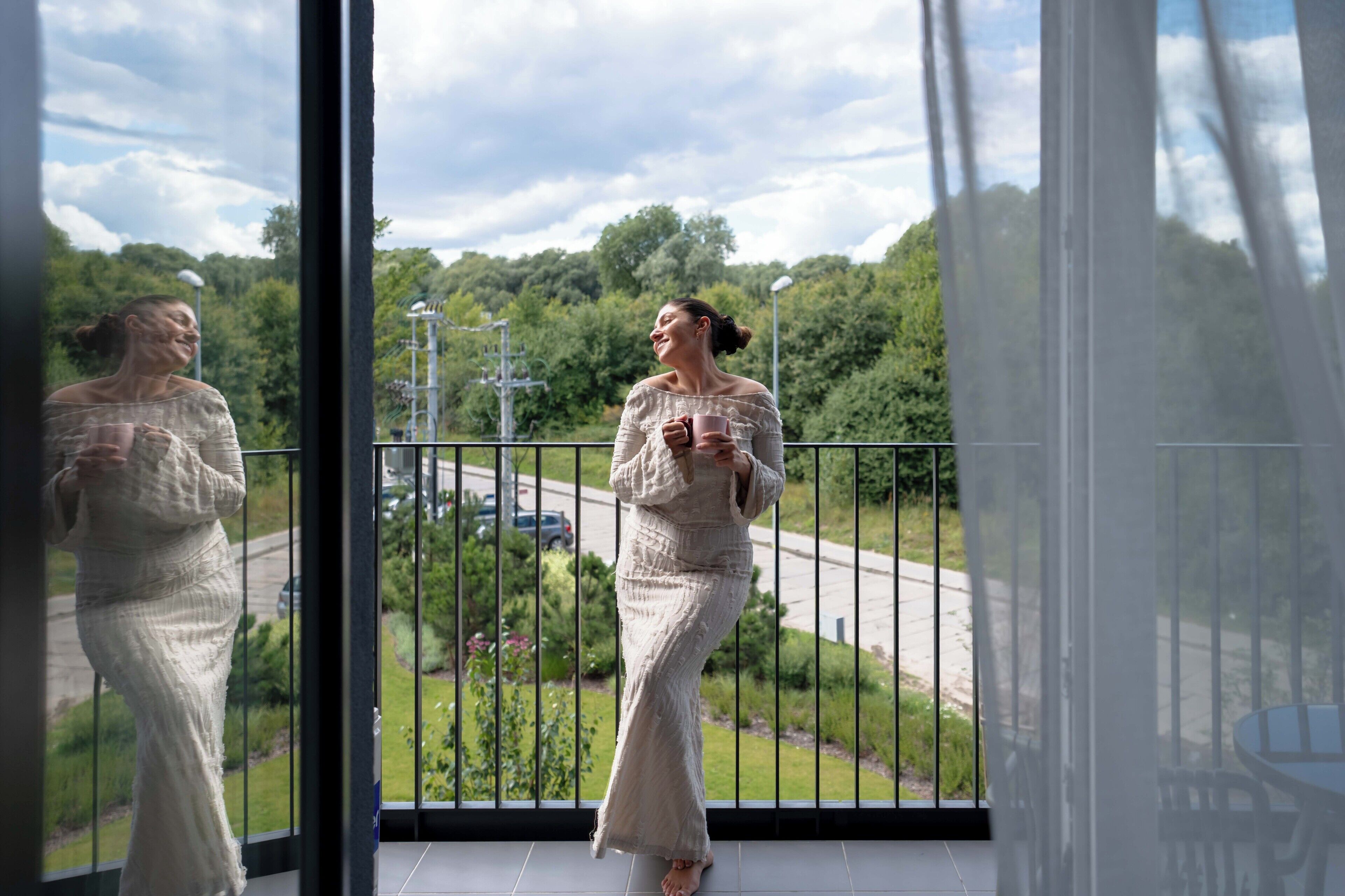 Eine Person steht auf einem Balkon mit Blick auf eine Straße und Grünflächen.