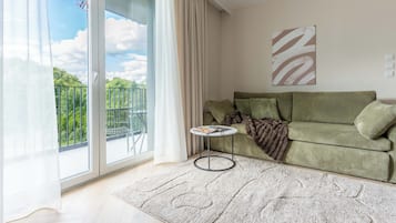 Una sala de estar con sofá, una mesita redonda y vistas a zonas verdes a través de un ventanal corredero.