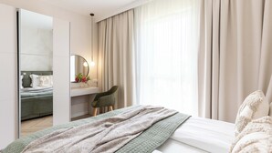 Ett hotellrum med en säng, ett skrivbord, en stol, en spegel och ett fönster med gardiner.