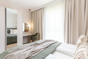 Ein Hotelzimmer mit Bett, Schreibtisch, Stuhl, Spiegel und einem Fenster mit Vorhängen.
