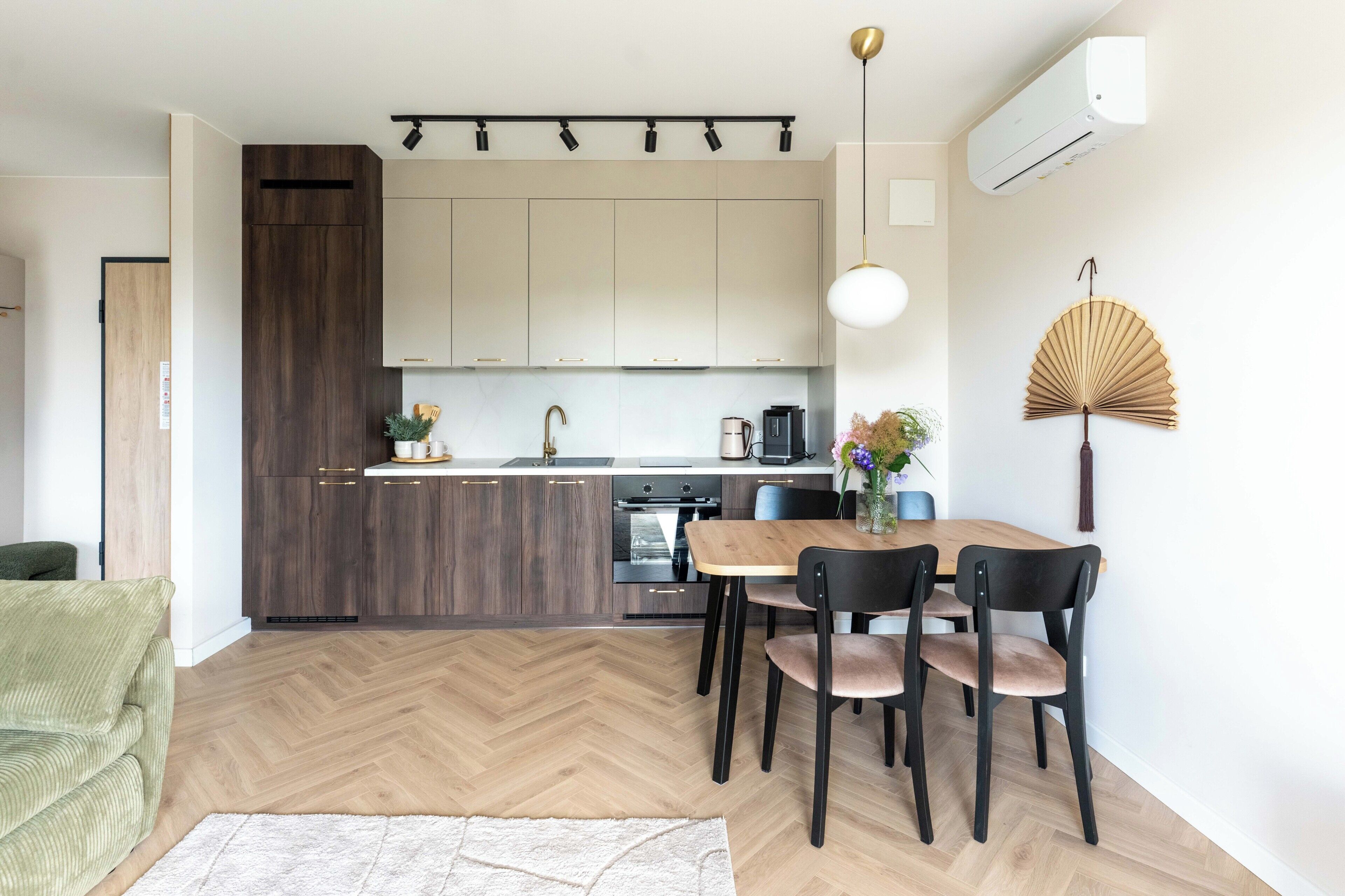 Une cuisine moderne avec un parquet en chevrons, un coin repas avec une table et des chaises en bois, et un ventilateur fixé au mur.