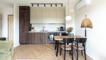 Une cuisine moderne avec un parquet en chevrons, un coin repas avec une table et des chaises en bois, et un ventilateur fixé au mur.