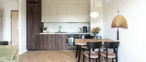 A modern kitchen with a herringbone floor, a dining area with a wooden table and chairs, and a fan on the wall.