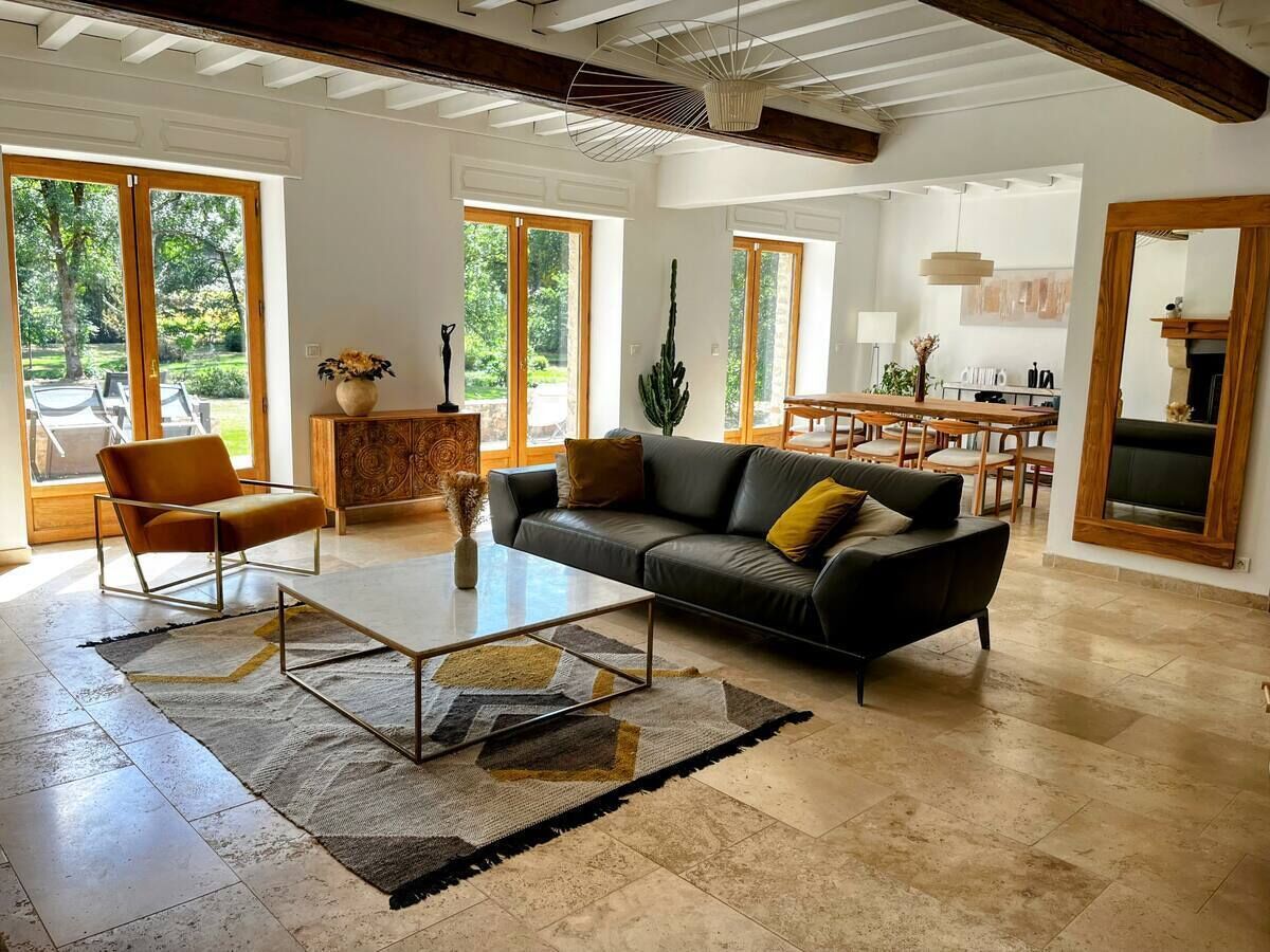 A spacious living room with a sofa, coffee table, and a chair. There is a large window providing a view of the outdoors.