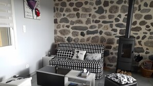 A cozy living room with a stone wall, a black and white patterned sofa, a white coffee table, and a black ottoman. - Maison Victoria - Haut-Allier: mountain view, balcony, countryside holiday rental (Saint-Bérain)