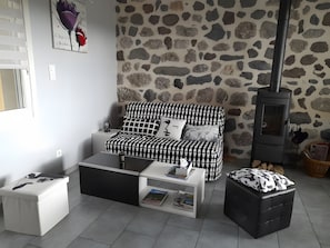 Una sala de estar acogedora con una pared de piedra, un sofá estampado en blanco y negro, una mesa de centro blanca y un reposapiés negro.