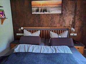 A bedroom with a bed, two bedside tables, a wall-mounted lamp, and a painting of a beach scene. - Vacation at Umlauf (Heringsdorf)