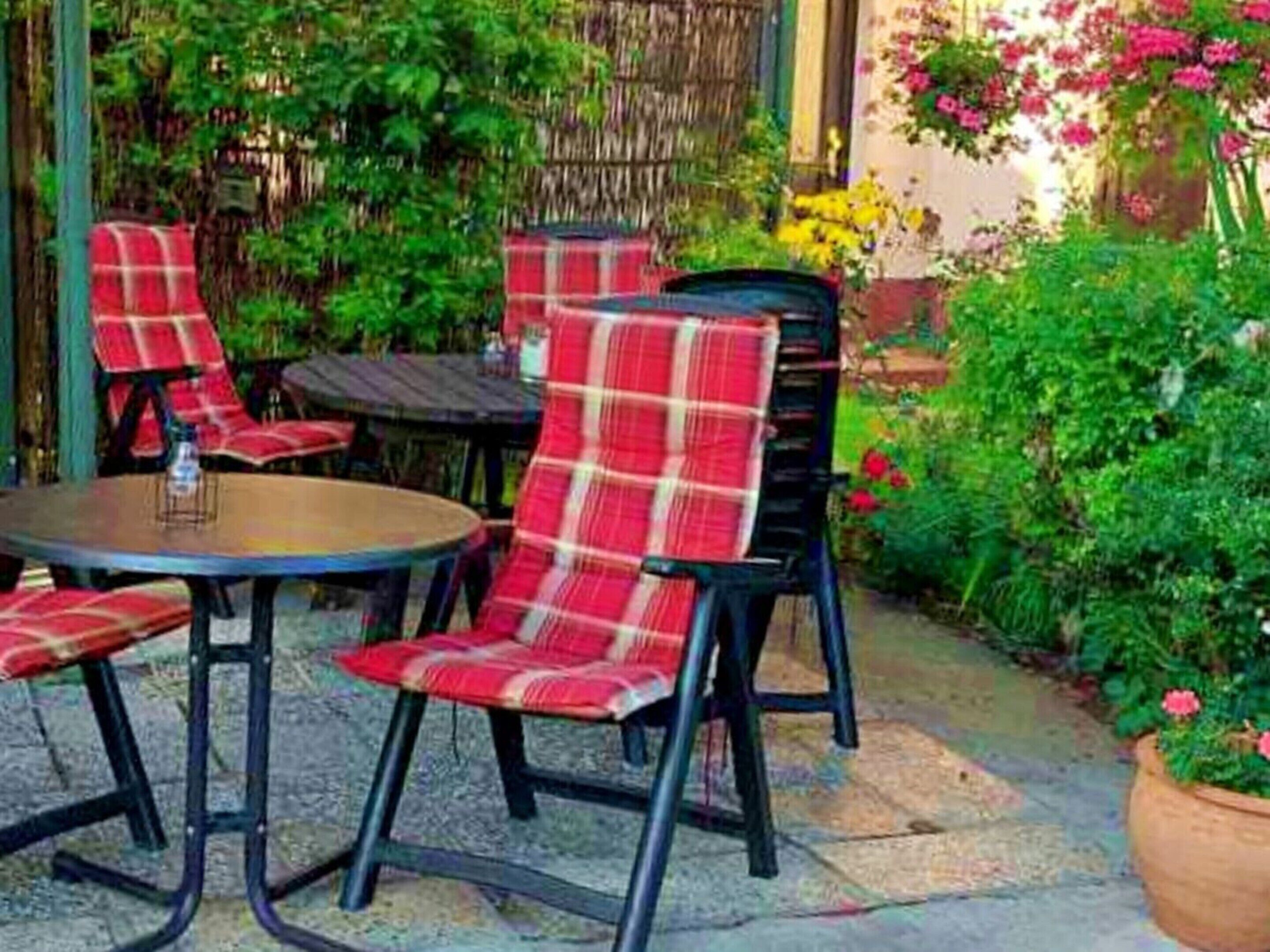 Un espace extérieur aménagé avec des tables et des chaises rondes, entouré d’une végétation luxuriante et de plantes en fleurs.
