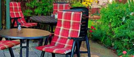 An outdoor seating area with round tables and chairs, surrounded by lush greenery and flowering plants.