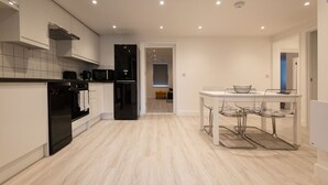 Una cucina moderna con mobili bianchi, un frigorifero nero e un'area pranzo con un tavolo in vetro e sedie.