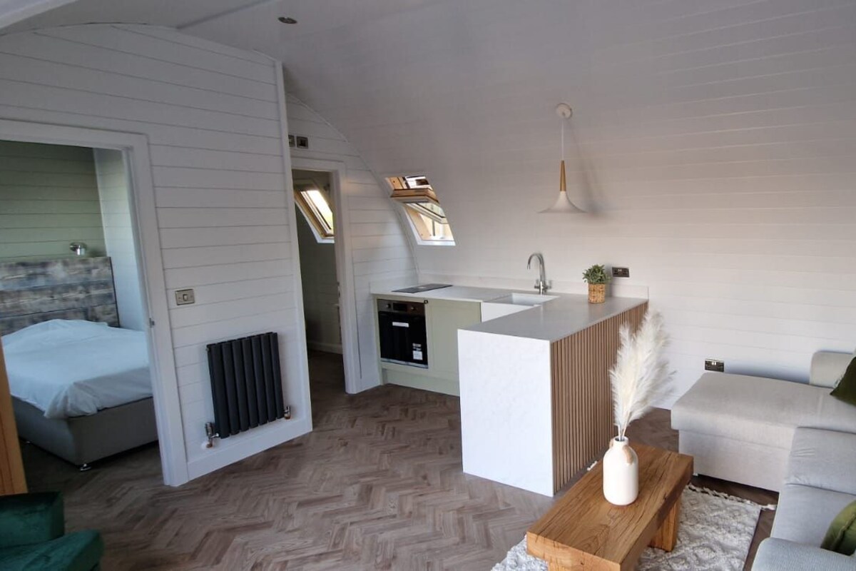 A compact living space with a kitchenette, a sofa, a small table, and a radiator.
