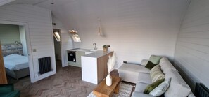 A compact living space with a kitchenette, a sofa, a small table, and a radiator. - The Bridge Collection (Brandon)