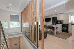 A modern kitchen with a dining area, a washing machine, and a staircase with glass railings. - The Bridge Collection (Brandon)