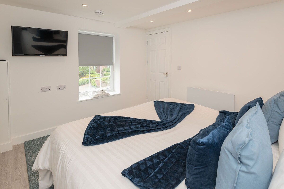 A bedroom with a bed, a television mounted on the wall, a window, and a door.