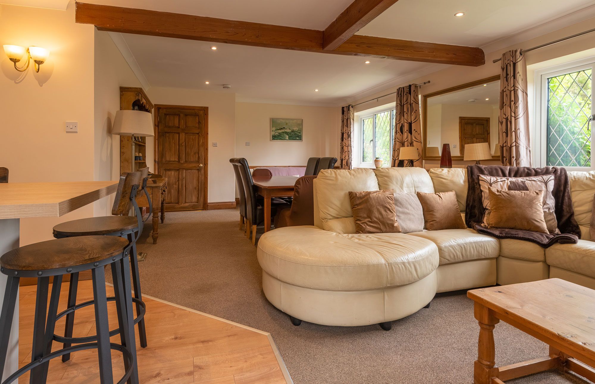 A cozy living room with a large L-shaped sofa, a wooden dining table, and a bar stool.