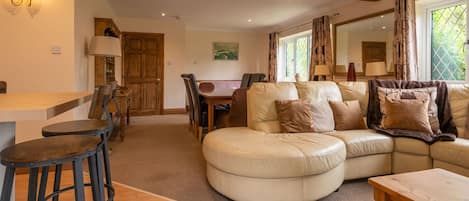 A cozy living room with a large L-shaped sofa, a wooden dining table, and a bar stool.