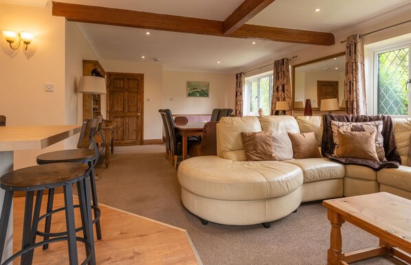 A cozy living room with a large L-shaped sofa, a wooden dining table, and a bar stool. - The Bridge Collection (Brandon)