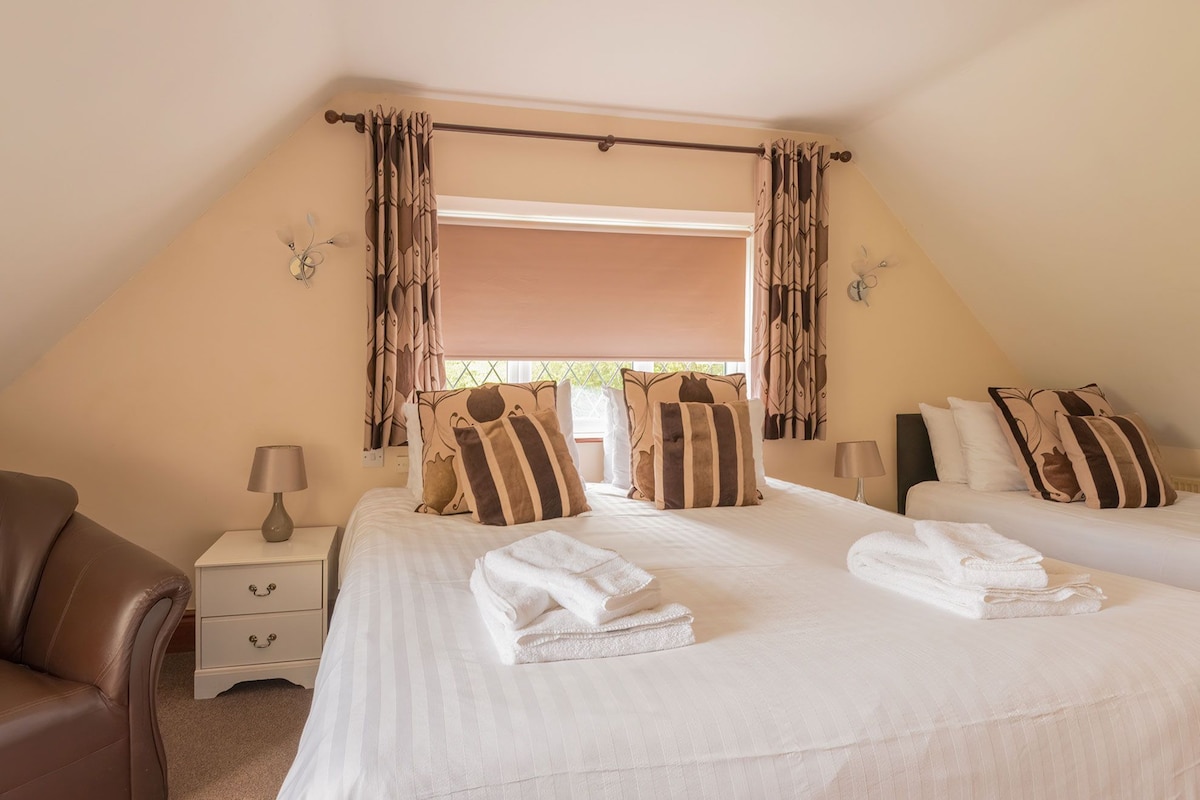 A bedroom with two beds, a nightstand, a lamp, and a window with curtains.