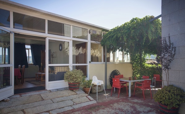 A residential building with a patio area featuring red chairs, potted plants, and a dining table.