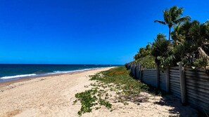 A beach with a wooden fence and palm trees, leading to the ocean. - Casa em Resort c 4 Su tes na Praia de Guarajuba (Camaçari)