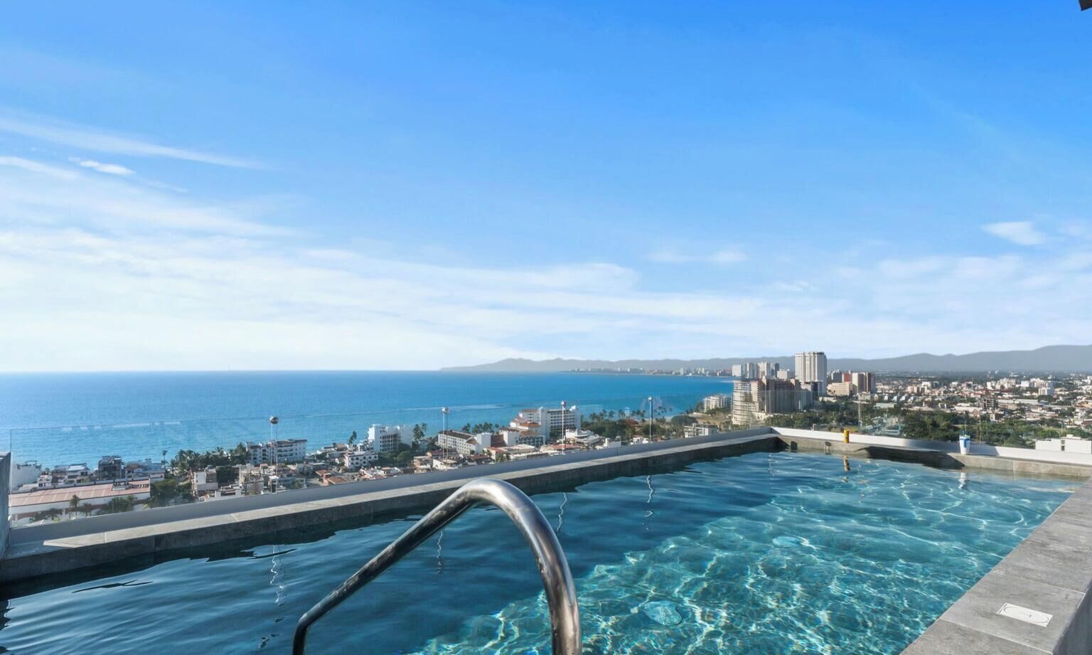 A rooftop infinity pool with a clear view of the ocean and cityscape.