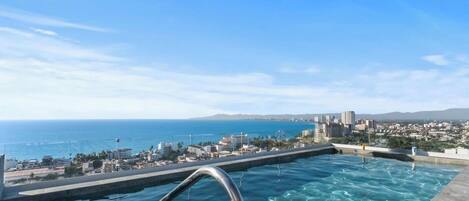 A rooftop infinity pool with a clear view of the ocean and cityscape.