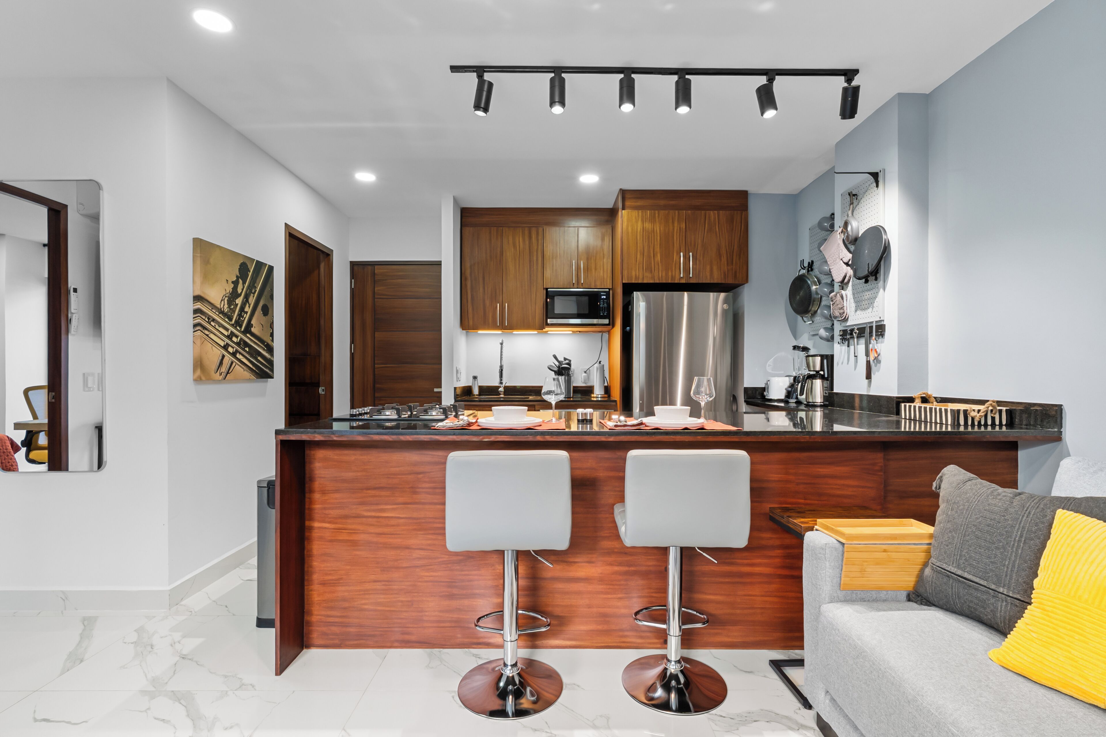 A modern kitchen with wooden cabinets, a stainless steel refrigerator, and a bar area with two stools.