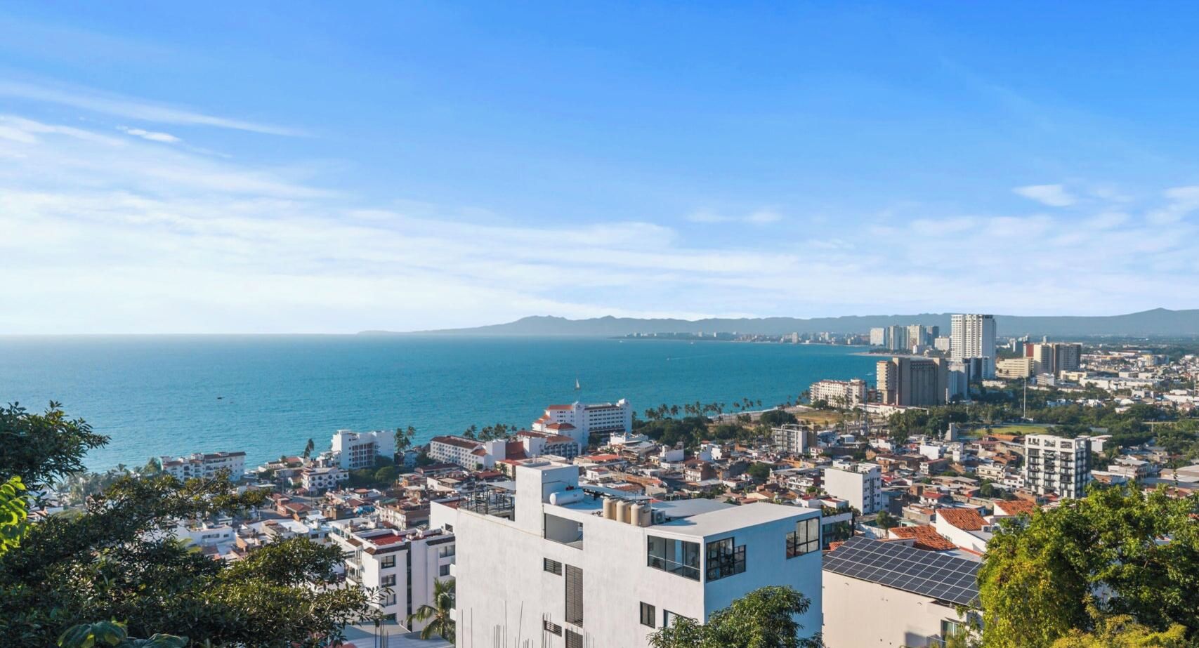 A coastal cityscape with buildings, a clear sky, and a view of the sea.