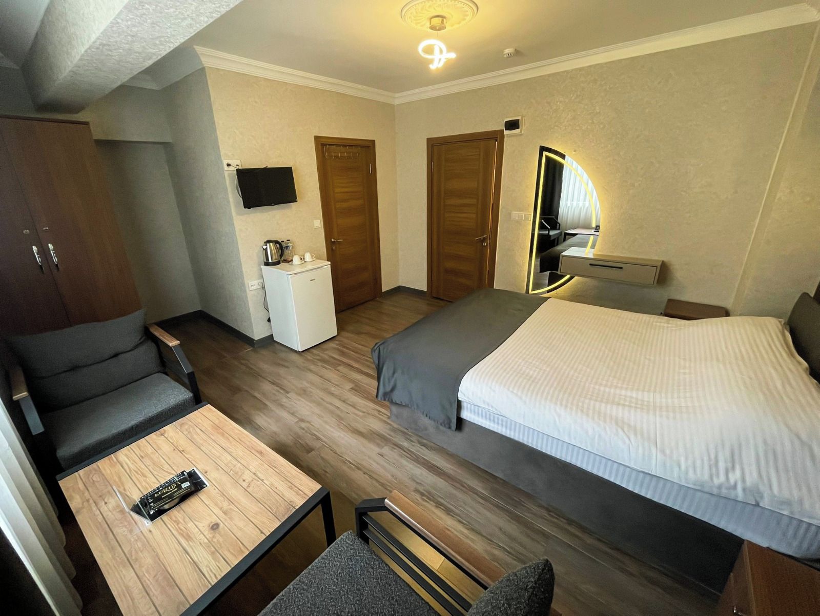 Habitación de hotel con cama, escritorio, silla, refrigerador pequeño, televisión y espejo.