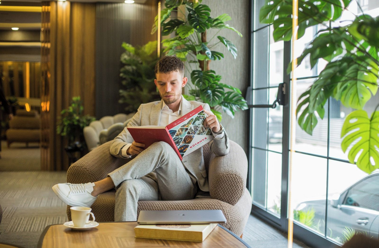Eine Person sitzt auf einem Sitzsack und liest ein Buch in einem modernen Innenraum mit großen Fenstern und Zimmerpflanzen.