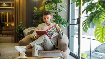 Eine Person sitzt auf einem Sitzsack und liest ein Buch in einem modernen Innenraum mit großen Fenstern und Zimmerpflanzen.