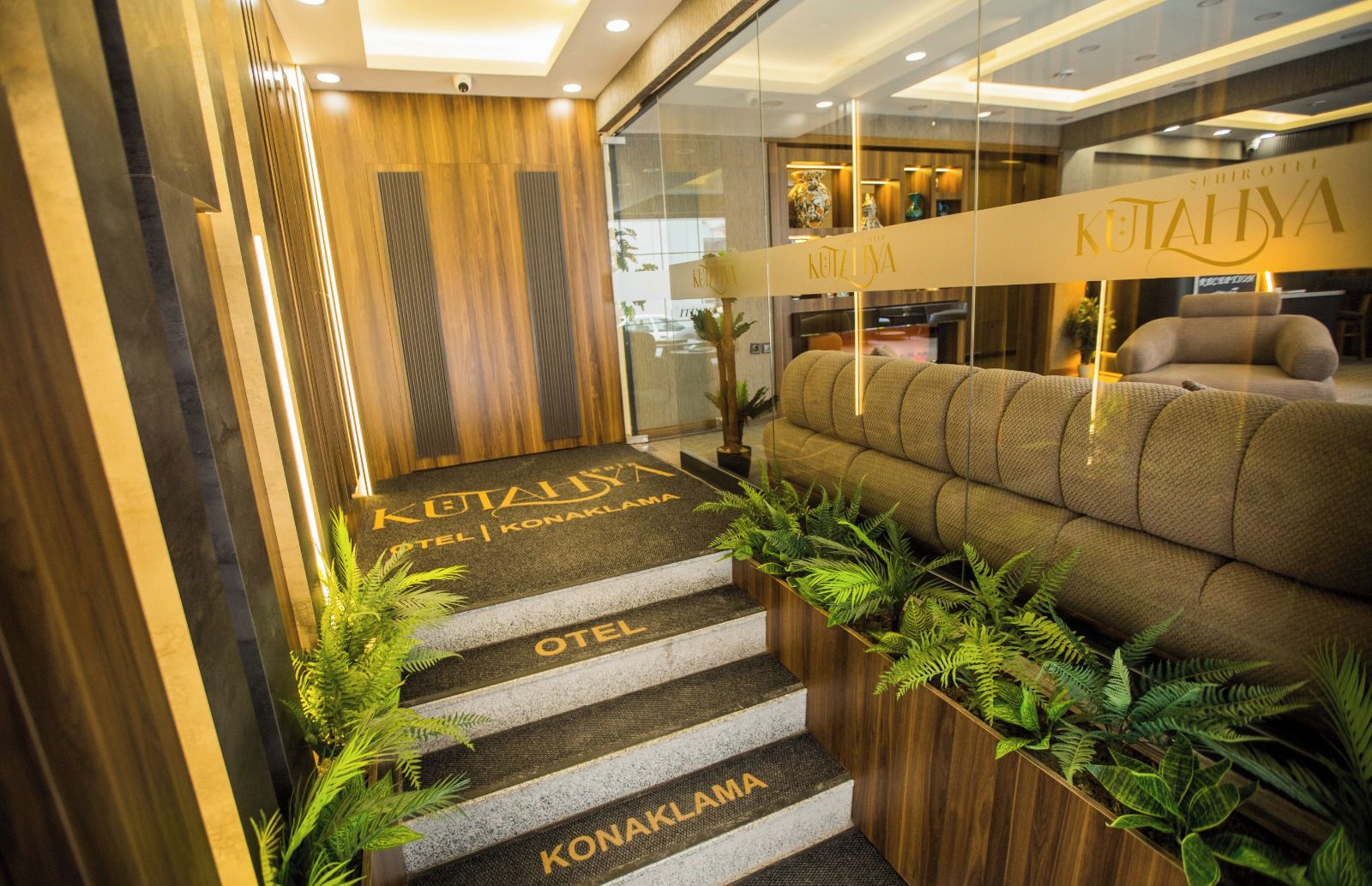 Un espace d’accueil d’hôtel comprenant un comptoir de réception, un canapé et un escalier menant aux chambres.
