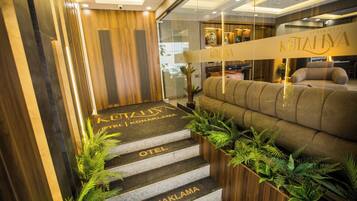 Un espace d’accueil d’hôtel comprenant un comptoir de réception, un canapé et un escalier menant aux chambres.