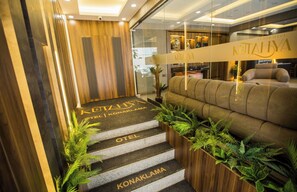 A hotel reception area with a reception desk, a sofa, and a staircase leading to the hotel rooms.