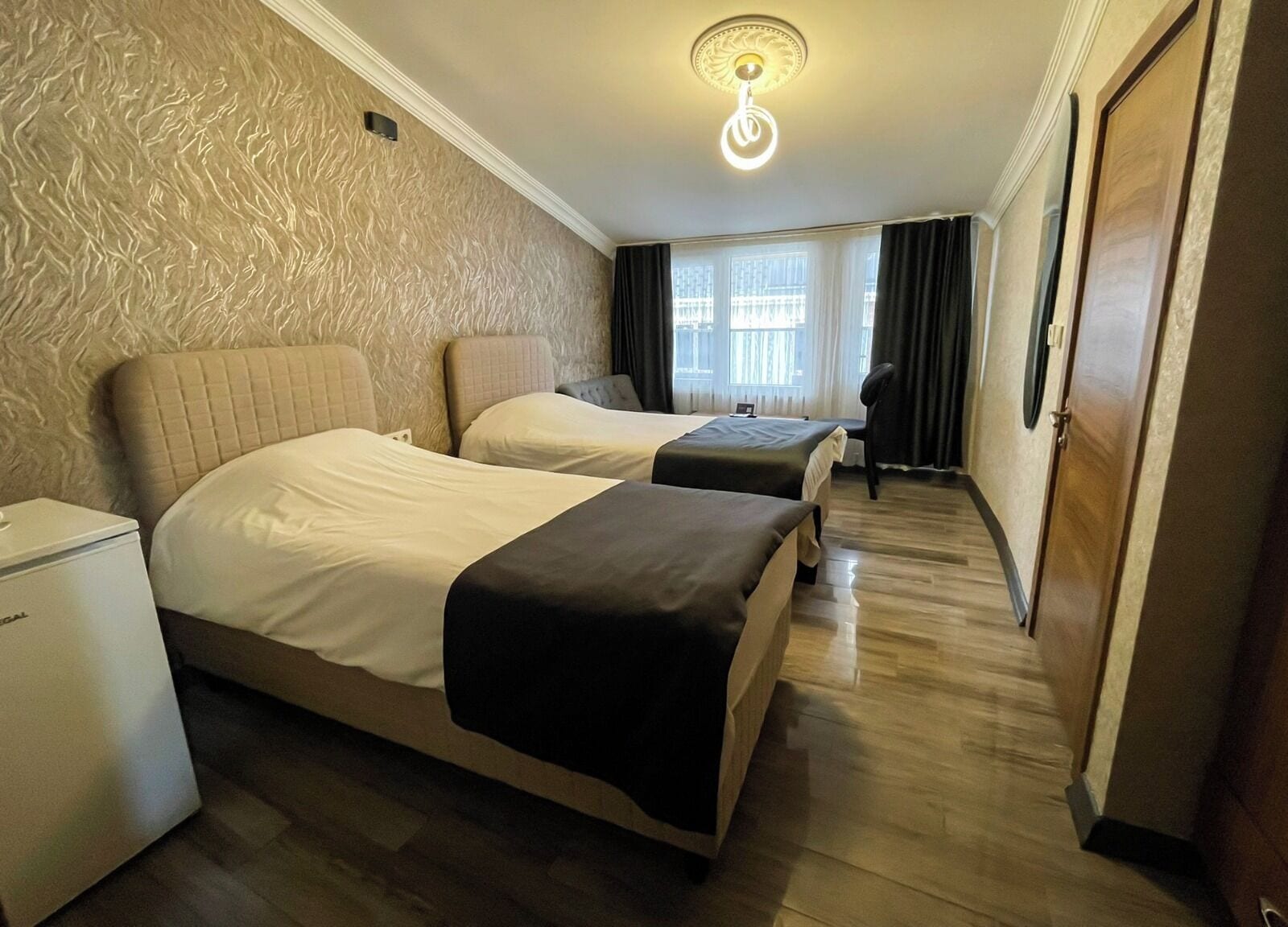 Une chambre d’hôtel avec deux lits, un petit bureau, une armoire et une fenêtre avec des rideaux.