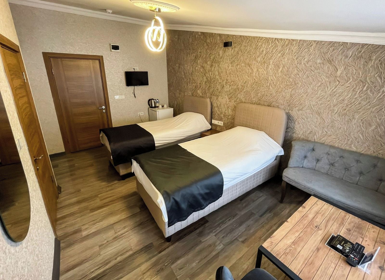 Habitación de hotel con dos camas, un sofá, una mesa de madera, un televisor y un calentador de pared.