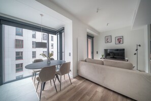 A modern living room with a sofa, TV, and dining area with chairs and a table. - Towarowa Towers Luxury Apartament | free parking (Warszawa)