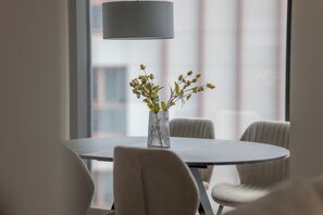 A round dining table with a clear glass vase containing yellow flowers, surrounded by upholstered chairs. - Towarowa Towers Luxury Apartament | free parking (Warszawa)