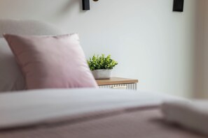 Valkoinen pääty ja vaaleanpunainen tyyny, ja pieni ruukkukasvi on sijoitettu puiseen yöpöytään.