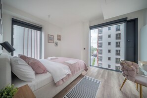 A modern bedroom with a bed, a bedside table, a window, and a view of a building outside. - Towarowa Towers Luxury Apartament | free parking (Warszawa)