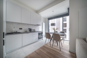 A modern kitchen with a dining area, featuring a large window, a built-in oven, and a dining table with chairs. - Towarowa Towers Luxury Apartament | free parking (Warszawa)