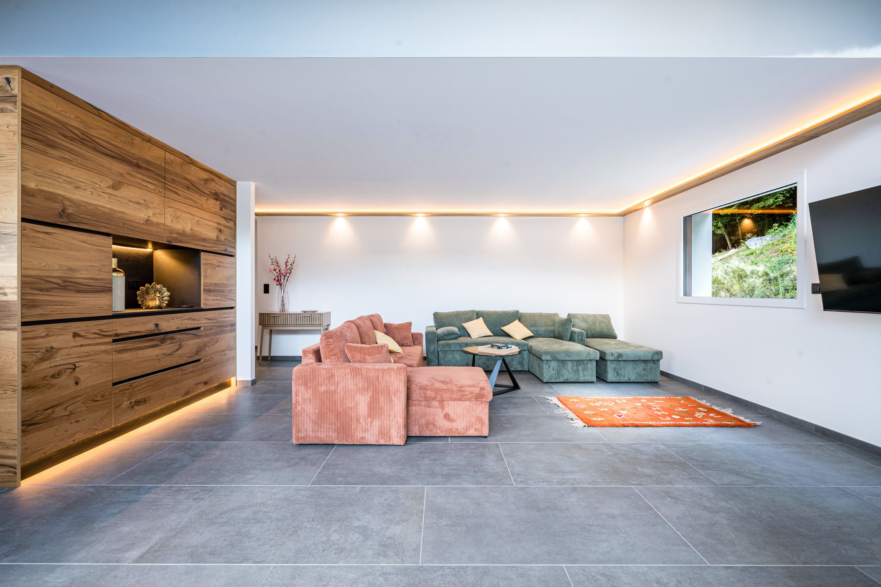 A modern living room with a sectional sofa, ottoman, and a flat-screen TV mounted on the wall.