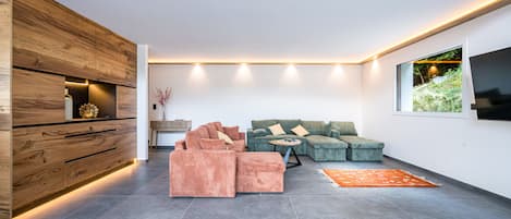 Una sala moderna con un sofá modular, un reposapiés y un televisor de pantalla plana montado en la pared.