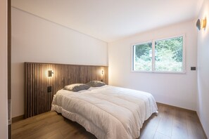 Une chambre à coucher avec une tête de lit en bois, un lit recouvert de linge de lit blanc et une fenêtre donnant sur un paysage verdoyant.