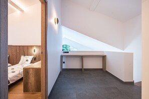 Ein modernes Interieur mit schrägverdeckter Decke, einem Bett mit Holz Kopfteil, einem kleinen Schreibtisch und Blick ins Grüne.