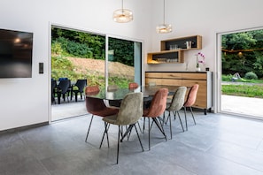 Ein moderner Essbereich mit einem Glastisch und Stühlen, einem Holzschrank und Blick auf einen angelegten Garten.