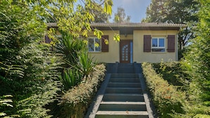 A house with a front entrance, a staircase leading up to the door, and a garden with various plants. - Le Buquet - Jardin clos de 700 m² (Elbeuf)