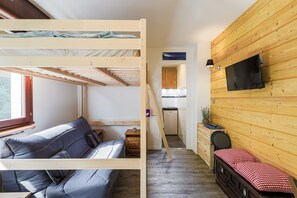 Een compacte kamer met een stapelbed, een kleine kitchenette en een televisie bevestigd aan de houten wand.