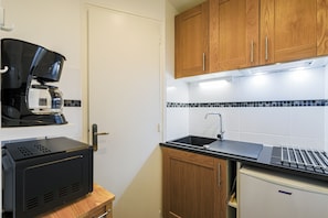 A compact kitchenette with a coffee maker, a small refrigerator, and wooden cabinets. - La Pause du Lindar - Studio avec Balcon (Aillon-le-Jeune)