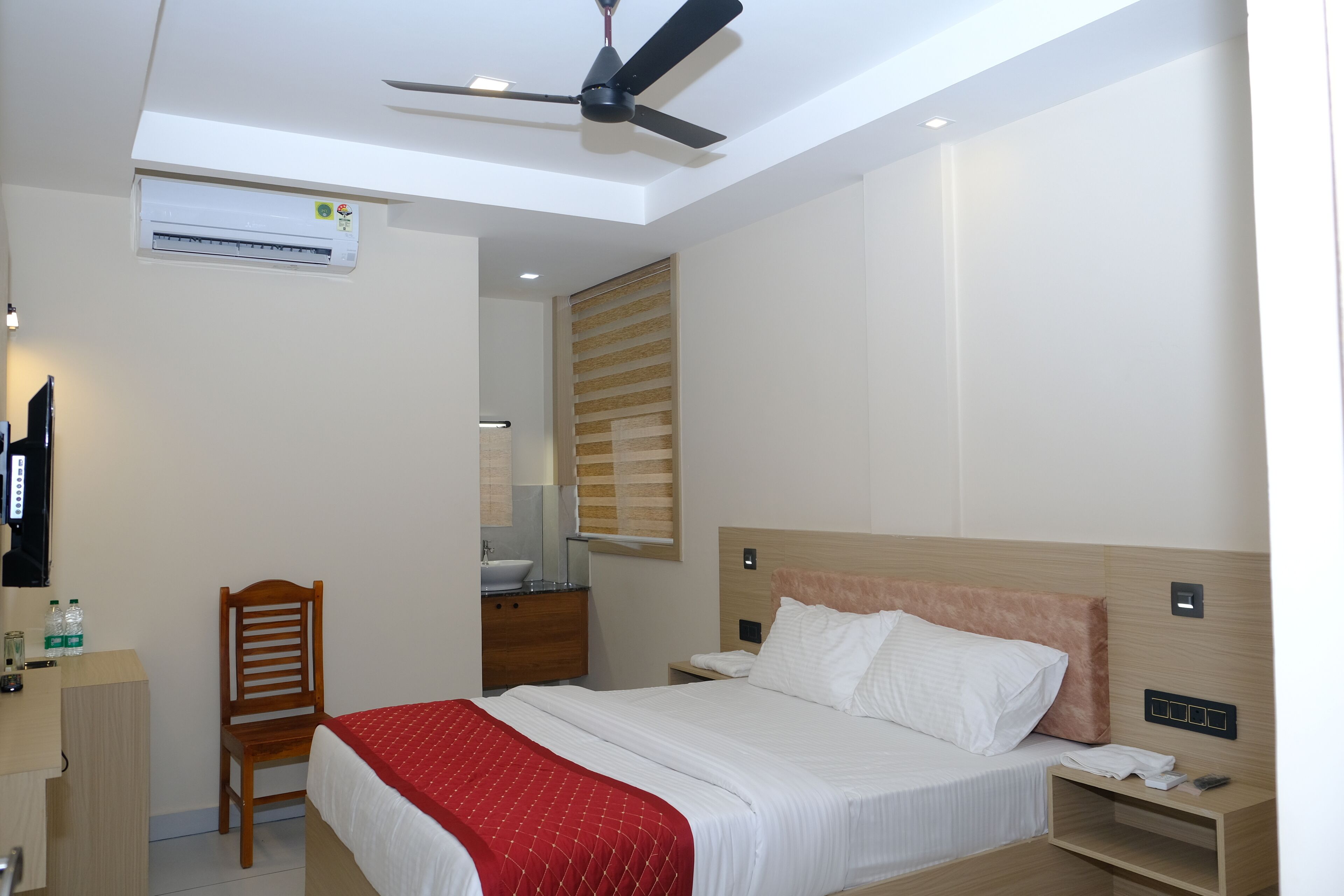 Habitación de hotel con cama, escritorio, silla, ventilador de techo y aire acondicionado.